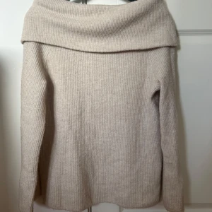 Beige offshoulder stickad tröja från H&M - Mysig beige stickad tröja från H&M med bred offshoulder-krage. Tröjan har lång ärm och är perfekt för kyligare dagar. Enkel att matcha med jeans eller kjol för en stilren look.