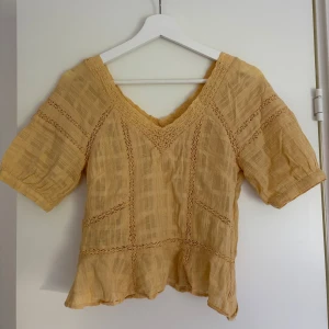 Gul blus med spetsdetaljer - Säljer en söt gul blus med v-ringning och fina spetsdetaljer. Blusen har korta ärmar och en lätt volang nertill. Perfekt för vår och sommar! 🌺🌺