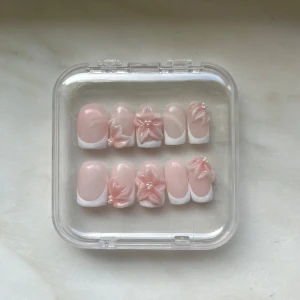 Press-on naglar med 3D-blommor 💗 - Säljer ett handgjorda set press-on naglar i ljusrosa med vit fransk tipp och 3D-blommor dekorerade med små pärlor. Naglarna har en square form och kommer i en genomskinlig ask. Lim ingår för enkel applicering. Tumme: 15mm, Pekfinger: 11mm, Långfinger: 12mm, Ringfinger: 10mm, lillfinger: 9mm (måtten är på ett ungefär) 💕
