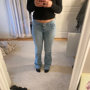 Ljusblå bootcut jeans med broderi - Säljer ett par ljusblå jeans med bootcut passform och snyggt broderi i rosa och vitt på bakfickorna. Jeansen har låg midja och klassisk femficksdesign. original pris 700kr
