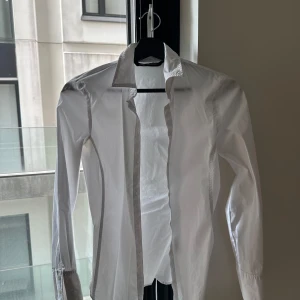 Vit skjorta från Zara XS tight - Klassisk vit skjorta från Zara i storlek XS. Skjortan har lång ärm, knappar framtill och en stilren krage. Perfekt för en clean och snygg look. Tillverkad i bomull för en skön känsla och bra passform.