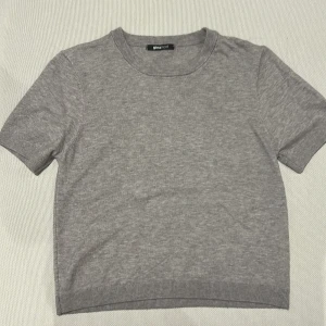 Grå kortärmad tröja Gina Tricot - En basic grå kortärmad tröja från Gina Tricot. Tröjan har rund halsringning och är tillverkad i mjukt stickat material. Perfekt att styla med jeans eller kjol för en clean look.                                 Sms för mer bilder på. 