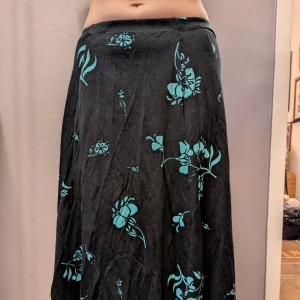 Svart långkjol med turkost blommönster - Flowig svart långkjol med turkosa blommor. Kjolen har en mjuk, skön material som passar bra för sommaren.