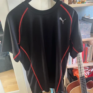Svart Puma T-Shirt - Svart t-shirt från Puma med röda sömmar längs axlar och sidor. Storlek S 🍒