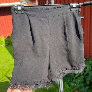 Svarta shorts med spets från Pieces - Svarta shorts från Pieces med elastisk midja och  volangkant och spetsdetaljer nertill. Iprincip oanvända. 