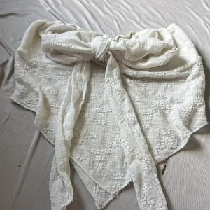 Vit bandeau tubtopp med knyt - Supersöt vit bandeau tubtopp med knyt framtill. Toppen har broderade små blommor och struktur i tyget, vilket ger en romantisk och trendig känsla. Perfekt till sommarens alla outfits och lätt att matcha med både kjol och jeans.