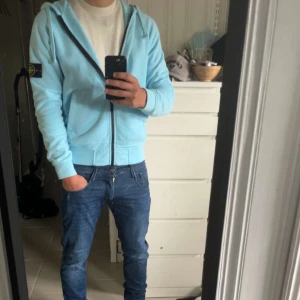 Ljusblå full zip hoodie från Stone Island - Säljer en ljusblå full zip hoodie från Stone Island med dragkedja och huva. 🩵Hoodien har klassisk patch på vänster ärm, 🪨🏝️såklart äkta köpt från sicuro.  Perfekt för dig som gillar ”grisch” looken och vill ha en clean look😍 Passar perfekt till dem neutrala färgerna väldigt unik, sjukt soft flis på insidan som inte är irriterande utan sjukt mjuk. Säljer då den inte kommer in i garderobs rotationen tillräckligt ofta knappt använd och inga defekter alls.🙂(priset inte hugget i sten)
