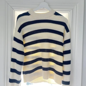 Randig stickad tröja från BikBok - Superfin stickad tröja från BikBok i vitt och mörkblått med breda ränder. Tröjan har en klassisk rund halsringning och långa ärmar. Perfekt för dig som gillar en chill och stilren look. Ribbstickade muddar vid ärmslut och nederkant. Använd 2-3 gånger, nyskick