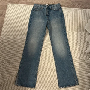 Blå raka jeans från Stradivarius med slits - Snygga blå jeans från Stradivarius med hög midja och raka ben. Jeansen har slitna detaljer vid fickan och slits nertill på benen. Aldrig använda då dom var för små, skulle säga att dom är lite långa i längden! Priset kan diskuteras!