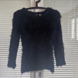 Svart fluffig tröja från Redoute - Supermjuk och fluffig svart tröja från Redoute Creation. Långärmad modell med rund hals och pälsliknande yta som ger en cool och mysig vibe. Perfekt för dig som vill sticka ut med en unik och trendig look.