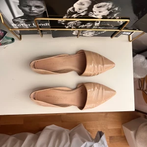 Beiga ballerinaskor från Kennel & Schmenger - Snygga ballerinaskor i beige lack från Kennel & Schmenger. Super bekväma med mjuk botten. Skorna har spetsig tå och platt sula, vilket ger en clean och modern vibe. Perfekta att styla med jeans eller klänning för en chic look. Ny pris ca 2 500kr