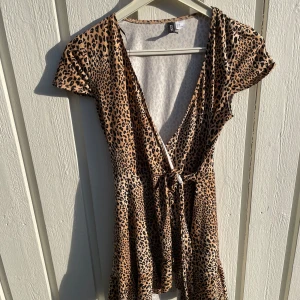 Leopardmönstrad omlottklänning H&M - Snygg kort leopardmönstrad klänning från H&M Divided. Omlottmodell med knyt i midjan, v-ringning och korta ärmar. Perfekt för dig som vill sticka ut med ett djurmönster och en feminin siluett.