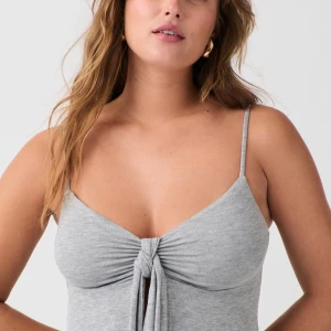 Grå linnetopp med knyt fram - Supersnygg grå linnetopp från Gina Tricot med smala axelband och knyt fram som ger en cool detalj. Mjuk och stretchig bomullsblandning, perfekt till jeans eller kjol. Toppen har en lätt v-ringad form och är lite croppad framtill.