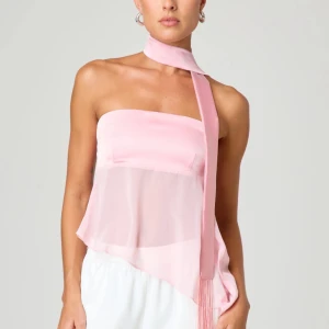 Ljusrosa bandeau tubtopp med scarf - Säljer en ljusrosa bandeau tubtopp med asymmetrisk nederkant och transparent tyg nedtill. Toppen har en matchande scarf som knyts runt halsen för en extra cool look. Perfekt för dig som vill sticka ut med en trendig och feminin stil. Jätte söt rosa topp med scarf 