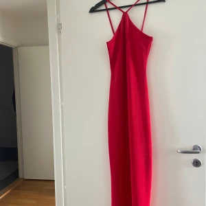 Röd långklänning från NA-KD XS - Snygg röd långklänning från NA-KD med smala axelband som korsas i ryggen. Klänningen har en tight passform och är ärmlös, perfekt för dig som vill sticka ut. Materialet känns mjukt och följsamt mot kroppen.