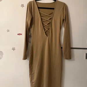 Beige långärmad klänning med snörning - Snygg beige långärmad klänning i bomull, polyester och spandex. Djup v-ringning framtill med cool snörningsdetalj. Kroppsnära passform och enkel design som ger en stilren look. Du kan hitta mer på min sida.