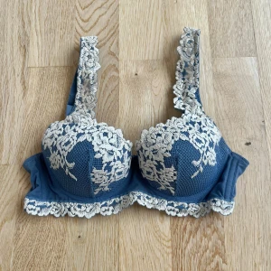 Blå Intimissimi BH - Supersnygg blå bh med vadderade kupor och vit blommig spets längs kanterna och axelbanden. Justerbara axelband och hakknäppning bak. Köptes på vinted för 300 kr. Jag har endast testat den och den har inga defekter!💞💞 skriv gärna vid funderingar!💞💞