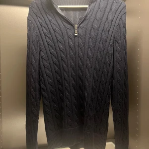 Mörkblå stickad half zip tröja - Mörkblå stickad tröja med kabelstickat mönster och half zip-dragkedja vid halsen. Tröjan har ribbade muddar och lång ärm, perfekt för lager-på-lager under kyliga dagar. Snygg och klassisk stil som funkar till det mesta. Nästan helt ny! Minns inte vart den e ifrån men tror nypris är 399 eller 499! Pris är diskuterat! 
