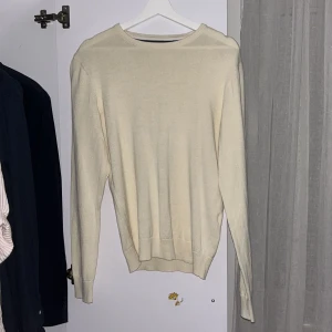 Beige stickad tröja från Pier One - En stilren beige stickad tröja från Pier One. Tröjan har rund halsringning, ribbade muddar och lång ärm. Perfekt för lager-på-lager och enkel att matcha med jeans eller chinos. Snygg och enkel design som funkar året runt.