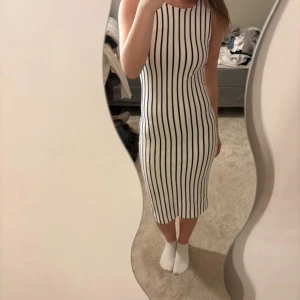 Randig klänning från Banana Republic - Snygg vit klänning med svarta vertikala ränder från Banana Republic Mad Men-kollektionen. Den är ärmlös, har en tight passform och en öppen ryggdetalj. Perfekt för dig som gillar stilrena och trendiga plagg med en twist.