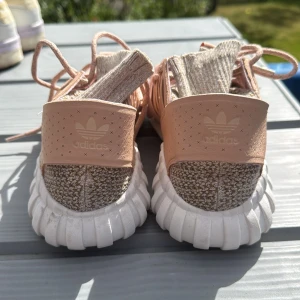 Adidas Tubular Shadow sneakers beige/rosa - Snygga Adidas Tubular Shadow sneakers i beige och ljusrosa med stickad ovandel och bred resår över foten. Skorna har vita, chunky sulor och snörning. Perfekta för dig som gillar en sportig och trendig look med sköna material och cool design.