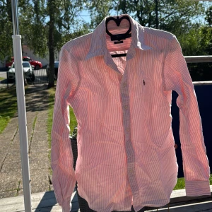 Rosa och vit randig skjorta Ralph Lauren - Säljer en snygg rosa och vit randig skjorta från Ralph Lauren, custom fit. Skjortan har klassisk krage, långa ärmar och knäppning framtill. Ikoniska broderade loggan på bröstet. Perfekt för dig som gillar preppy stil.