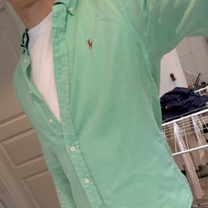 Mintgrön Polo Ralph Lauren Skjorta - Väldigt fräsch mintgrön skjorta från Ralph Lauren i slim fit-modell, storlek S. Klassisk oxfordskjorta med knappar hela vägen, button down-krage och broderad logga på bröstet. Tillverkad i 100% bomull för en skön känsla och snygg passform. Riktigt härligt färg, perfekt till sommaren!