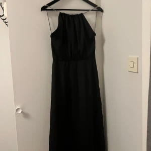 Svart klänning - Oanvänd svart klänning i glansigt material med fina detaljer som tunna silverfärgade kedjeband som axelband 🤍