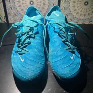 Nike Phantom GX PRO BLÅ - Nike Phantom GT2 fotbollsskor i en fräsch blå färg med vita detaljer och snörning. Skorna har en strumpliknande passform och är tillverkade i syntetmaterial för bästa grepp och kontroll på planen. Perfekta för dig som vill sticka ut på fotbollsplanen.