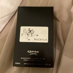 Creed Aventus 120ml parfym - Lyxig parfym Creed Aventus i 120ml flaska. Flaskan är genomskinlig med svart etikett och silverdetaljer, samt en svart kork. Märkets logga och ryttare syns tydligt på både kartong och flaska. Kommer med originalförpackning och informationsblad.