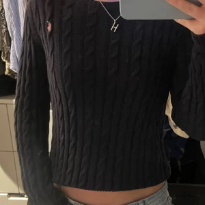 Mörkblå kabelstickad tröja Ralph Lauren - Säljer en mörkblå kabelstickad tröja från Ralph Lauren. Tröjan har lång ärm och en  rosa logga broderad på bröstet. Tröjan är i storlek 17 år men passar mig som brukar ha xs/s. Har bara använts ett fåtal gånger, bilden är lånad men finns fler om det önskas. Men pris går att diskutera (Nypriset är ca 1500 kr)