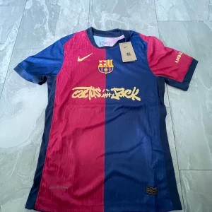 FC Barcelona x Travis scott - Säljer en FC Barcelona matchtröja i blått och rött som är en kollab med Travis scott. Tröjan har korta ärmar, Dri-FIT material och tryck med 'Cactus Jack' samt UNHCR-logga på ryggen. Perfekt för dig som älskar Barca och vill sticka ut på planen.