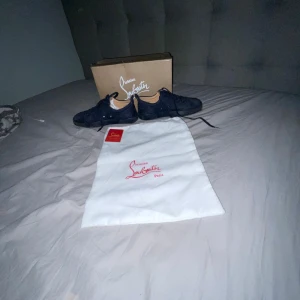 Svarta sneakers från Christian Louboutin (ÄKTA) - Säljer ett par blåa sneakers från Christian Louboutin med klassisk röd sula. Skorna har snörning och är tillverkade i mocka. Kommer med originalkartong och dustbag.(ÄKTA)