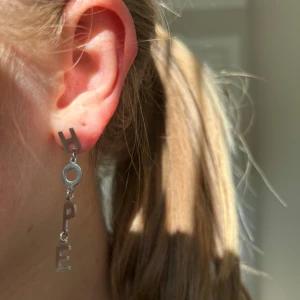 Ioaku örhängen  - Säljer ett coolt örhänge i silverfärg där bokstäverna H-O-P-E hänger lodrätt. Perfekt statement piece för dig som vill ha något unikt och personligt. Passar till många olika stilar och tillfällen. Använd fåtal gånger.