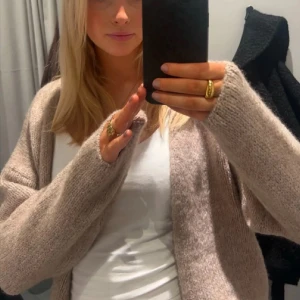 Beige stickad kofta - Mysig beige stickad kofta med lång ärm och öppen framtill. Perfekt att slänga på sig över en t-shirt för en avslappnad look. Koftan har en mjuk och fluffig känsla och passar till många olika outfits.