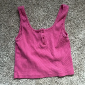 Rosa ribbad linnetopp från Gina Tricot - Säljer en rosa ribbad linnetopp från Gina Tricot. Toppen har en croppad passform och knappar framtill. Perfekt för varma dagar och enkel att matcha med jeans eller shorts.