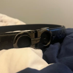 Svart skärp från Ferragamo med silverdetaljer - Säljer ett svart bälte från Ferragamo i storlek 120cm . Skärpet är skin och bucklan är i silver 9/10 skick använd fåtal gånger hör av er vid minsta fundering.