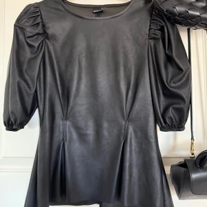 Svart läderblus - Säljer en svart blus i skinnimitation från Gina Tricot. Blusen har puffiga ärmar med resår vid ärmslut och en rund halsringning.