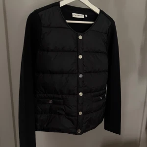Svart cardigan med knappar från Ps Of Sweden - Snygg svart dunväst från Ps med rund halsringning och knäppning framtill. Västen har quiltad framsida med dekorativa knappar och två fickor. Ärmar och baksida i mjukt tyg för en modern look. Så gott som ny i stl S, den finns inte längre att få tag på deras hemsida💕