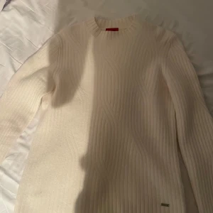 Vit stickad tröja från Hugo Boss - Säljer en stilren vit stickad tröja från Hugo Boss. Tröjan har rund halsringning, ribbad struktur och långa ärmar. Perfekt för lager-på-lager och enkel att matcha med olika outfits.