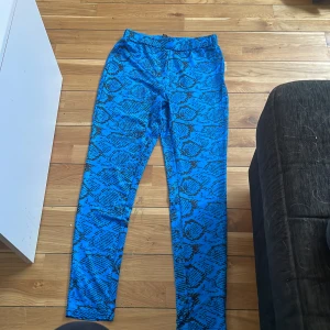Blå leggings med ormmönster - Säljer ett par blå leggings med svart ormmönster. Byxorna har en tight passform och är tillverkade i ett stretchigt syntetmaterial. Perfekta för dig som vill sticka ut med ett unikt mönster.