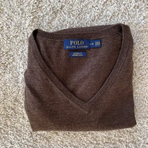 Brun v-ringad tröja från Polo Ralph Lauren - Snygg brun v-ringad tröja från Polo Ralph Lauren i mjuk merinoull. Klassisk modell med långa ärmar och diskret logga på bröstet. Perfekt för en stilren och tidlös look.