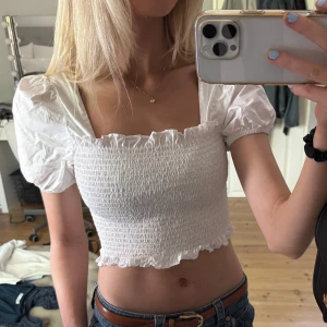 Vit croppad topp från Glamorous - Säljer en söt vit croppad topp från Glamorous med puffärmar. Toppen har volangdetaljer vid ärmslut och nederkant samt fyrkantig ringning. Perfekt för varma dagar!