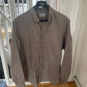 Beige linneskjorta från Cubus - Säljer en brun långärmad skjorta från Cubus i 100% linne. Skjortan har klassisk krage, knäppning framtill och en avslappnad regular fit. Perfekt för dig som gillar stilrena och svala plagg. Nypris 600kr