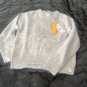 Ljusgrå stickad tröja från Lager 157 - Nyköpt med prislapp kvar för att den var för liten! Säljer en ljusgrå stickad tröja från Lager 157 med rund halsringning och ribbade muddar vid ärmslut och nederkant.