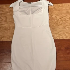 Vit tight klänning från NLY One - Säljer en stilren vit klänning från NLY One med fyrkantig ringning och breda axelband. Klänningen är tight och har en enkel, elegant design som passar perfekt till speciella tillfällen.