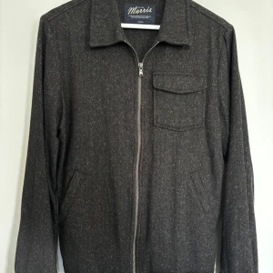 Mörkgrå jacka med dragkedja från Morris - Snygg mörkgrå jacka från Morris i storlek small. Jackan har dragkedja framtill, en bröstficka med lock och två snedställda fickor. Klassisk krage och diskret mönster i tyget ger en stilren look. Helt oanvänd. Nypris 1 900 kr, pris kan diskuteras 