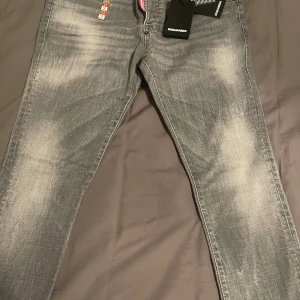 Grå jeans från Dsquared2 - Snygga grå jeans från Dsquared2 med slitna detaljer och klassisk femficksmodell. Jeansen har en rak passform och tydliga tvättade partier framtill och baktill. Perfekta för dig som gillar streetwear och vill sticka ut lite extra. Aldrig använt.