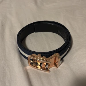 Blått och vitt bälte från William Manor - Snyggt bälte från William Manor i blått med en vit rand och ett stilrent spänne i guld. Bältet har en modern design och passar perfekt till jeans eller chinos. Levereras i originalförpackning med användarguide. Funkar nog för de flesta då jag har stor midja och man klipper det baserat på hur man vill att det sitter 