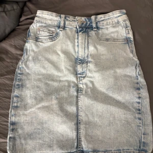 Ljusblå jeanskjol från Gina Tricot - Säljer en ljusblå jeanskjol från Gina Tricot, modell Molly. Kjolen har klassisk femficksdesign, bälteshällor och knappstängning framtill. Snygg, rak passform och perfekt för en trendig vardagslook.